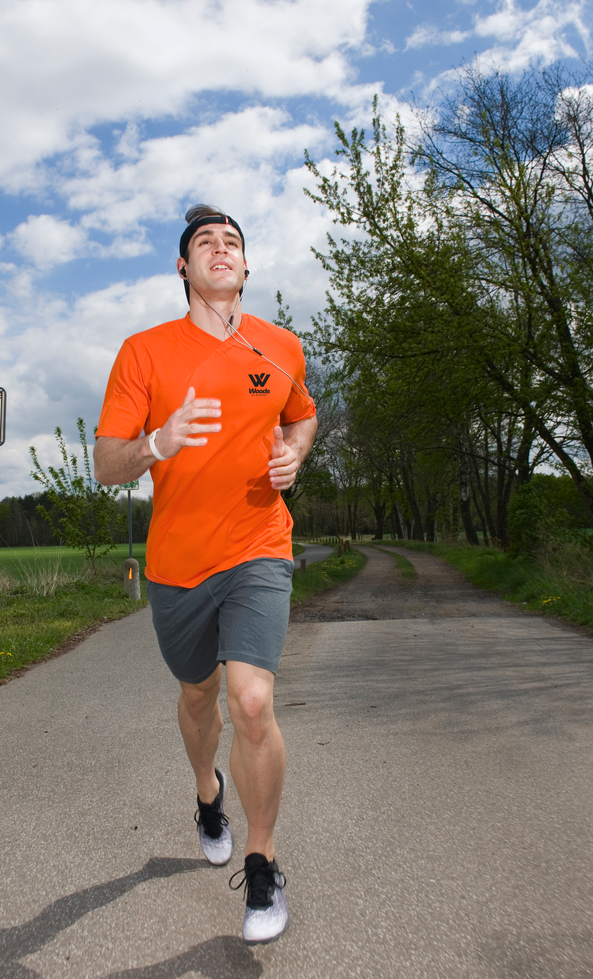 Photo shows a young man running along a country road wearing an orange Woods running shirt