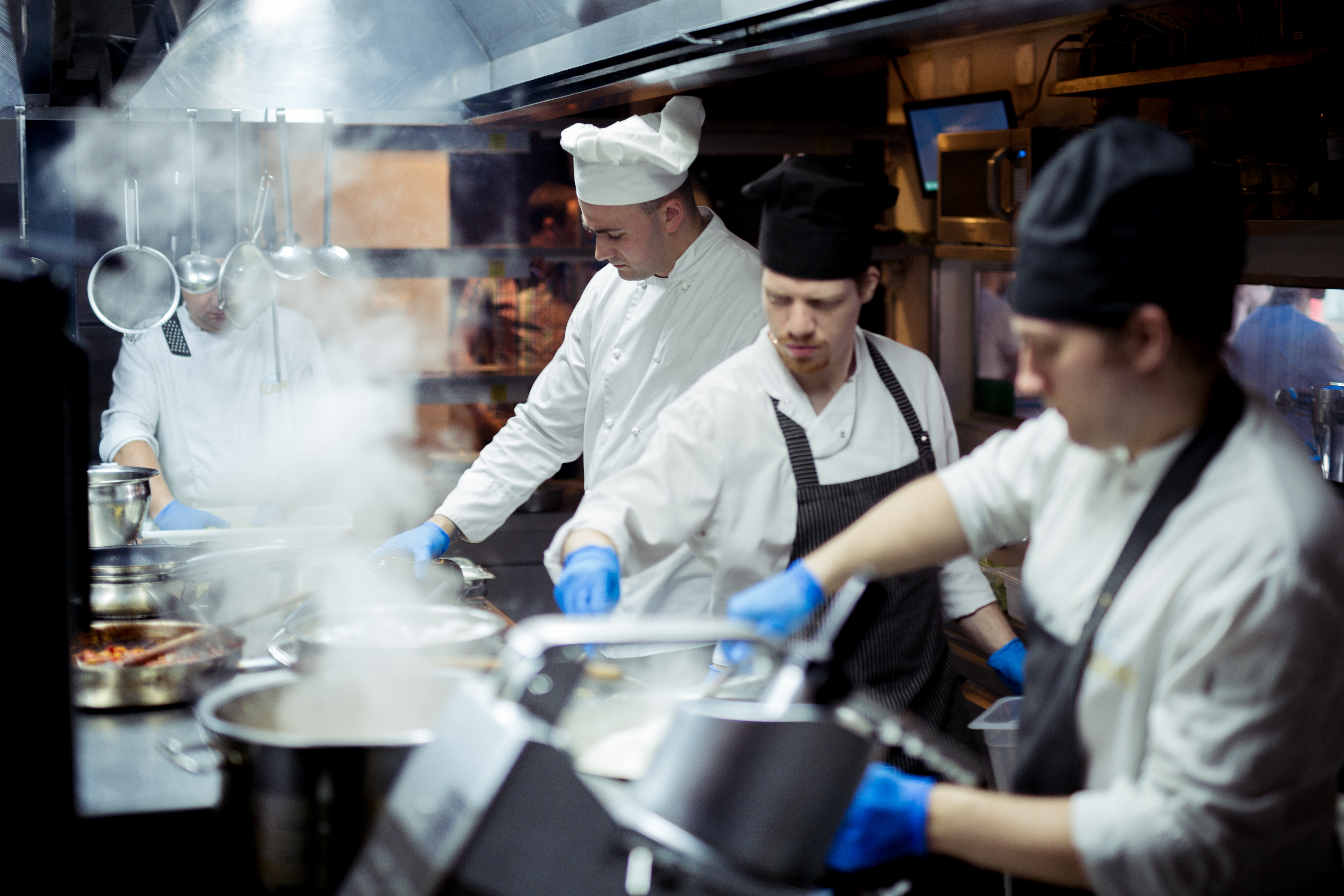 Photo shows three chefs working together in a steamy kitchen