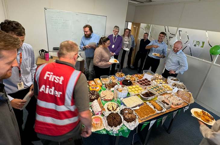 Woods staff gathered around a table loaded with sweet and savoury treats for Macmillan Coffee Morning